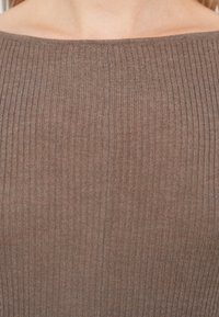 Parte superior de punto acanalado marrón con escote estilo off-shoulder. La tela muestra una textura suave con líneas verticales y una silueta ajustada.