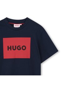 Navy μπλουζάκι από βαμβάκι με κόκκινο ορθογώνιο λογότυπο που αναγράφει "HUGO" σε μαύρο. Λαιμόκοψη crew και κοντά μανίκια.