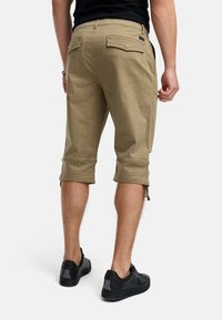 Shorts cargo kaki avec ourlets retroussés, poches arrière et pattes latérales ajustables. Portés avec des baskets noires sur un fond uni.