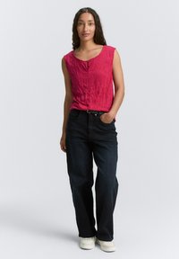 Top rose sans manches avec texture froissée et détail de bouton, associé à un jean large bleu foncé et des baskets blanches.