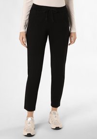 Pantalones jogger negros ajustados, confeccionados con una tela suave, que cuentan con una cintura elástica con cordón y bolsillos laterales. Complementados con zapatillas beiges.