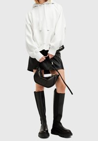 Witte hoodie met een losse pasvorm, zwarte leren minirok, zwarte handtas en kniehoge zwarte laarzen met dikke zolen.