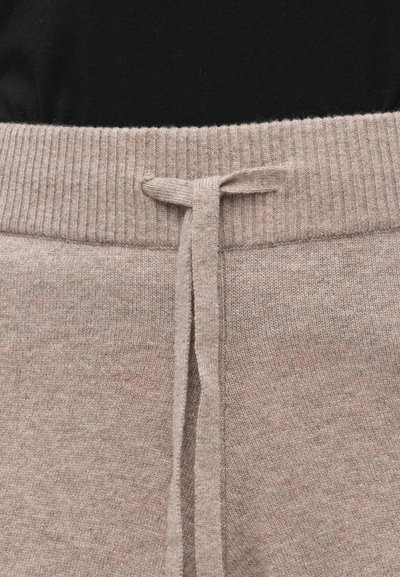 Beežid kootud dressipüksid soonikkoes vöökohaga ja nöörkinnitusega. Textuurse kangaga, millel on peen kirju muster. Vöökohast lähedalt vaadatuna.