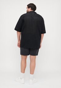 Svart t-skjorte med kort erm og avslappet passform, ryggen med spennende detaljer, kombinert med mørkegrå shorts og hvite joggesko. Glatt tekstur, uformelt design.