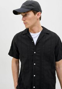 Kortärmad svart skjorta med knappstängning fram, med en texturerad tyg och subtila vertikala ränder, bärs över en vit T-shirt.