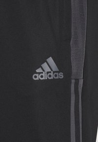 Svarta idrottsbyxor med Adidas-logotyp i grått. Har en texturerad sido panel och tre vertikala grå ränder längs sömmarna.