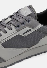 Gray sneakers with a mix of matte and textured materials, featuring subtle branding, contrasting overlays, and a patterned side panel.