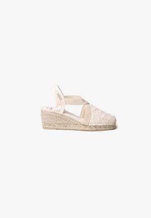 Espadrille compensé tissé beige avec une sangle ajustable et un tissu texturé. Comprend une semelle intermédiaire en corde naturelle et une semelle extérieure en caoutchouc pour une meilleure traction.