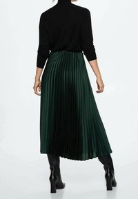Green pleated maxi skirt with a high waistband, made of smooth, flowing fabric, paired with fitted black turtleneck and sleek black boots.