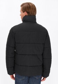 Sort puffjakke med høj krave, der har vandrette quiltede sektioner og en glat, mat overflade. Båret med denimjeans.