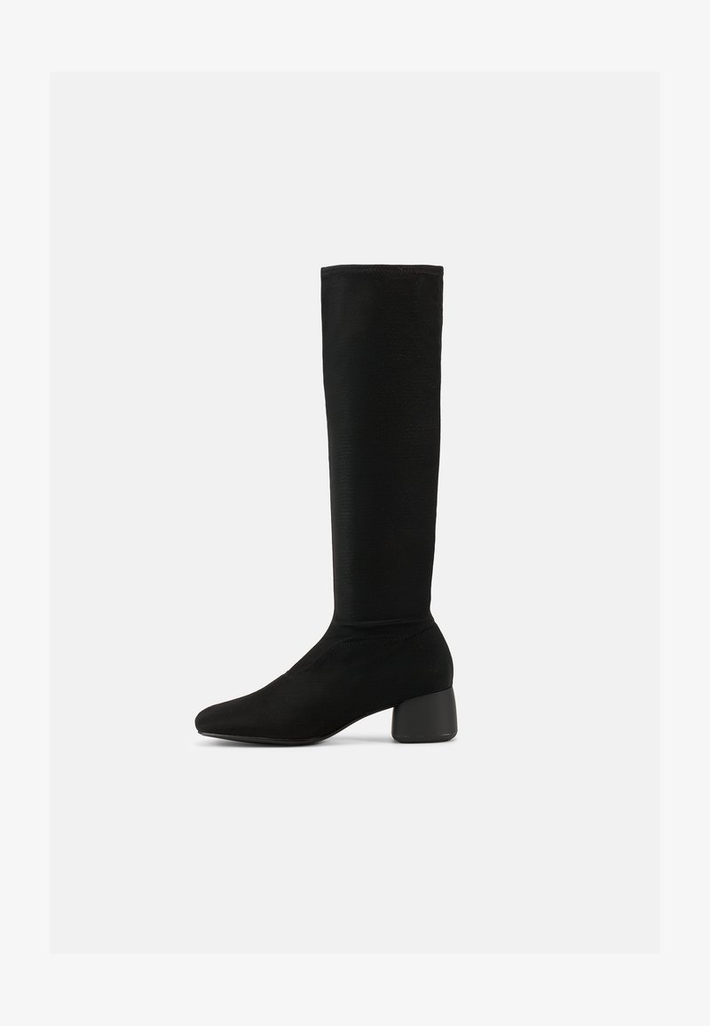 Μαύρη ελαστική μπότα μέχρι το γόνατο με στρογγυλεμένο τακούνι μπλοκ και ελαφρώς μυτερή μύτη, εμφανίζεται από το πλάι σε λευκό φόντο.