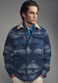 Navy jacket with a textured pattern in shades of blue, featuring a soft beige collar, front pockets, and a button closure.