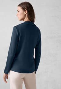 Marinblus med långa ärmar och skarp krage, med en slät textur, som har en figursydd design och diskret elegans.