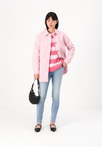 Light pink wool coat with buttons, striped pink and white knitted sweater, light blue jeans, black perforated handbag, and black flats.