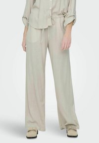Světlý béžový outfit z lněné směsi, který zahrnuje volně střiženou košili s ohrnovacími rukávy a široké kalhoty v matching barvě. S elastickým pasem a hladkou texturou.