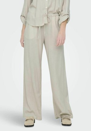 Světlý béžový outfit z lněné směsi, který zahrnuje volně střiženou košili s ohrnovacími rukávy a široké kalhoty v matching barvě. S elastickým pasem a hladkou texturou.