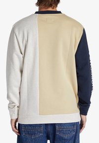 Sudadera con bloques de color que presenta paneles en gris, beige y marino. Material suave con cuello de canalé y texto impreso en la manga.