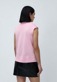 Kortermet, rosa strikket topp med krage, med en jevn tekstur og ribbet nederkant, kombinert med et svart skinn mini-skjørt.