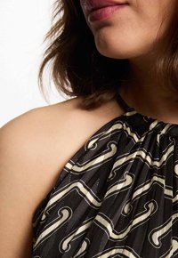 Schwarzes Haltertop mit einem gemusterten Design in Creme, aus gerafftem Stoff und mit glatter Textur. Die Details umfassen den Ausschnitt und den Schulterbereich.
