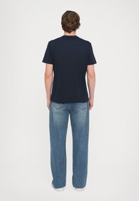 Maglietta a maniche corte blu navy abbinata a jeans a gamba larga azzurri, con vestibilità comoda e orlo dritto. Design minimalista senza motivi.