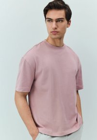 Světle růžové tričko s kulatým výstřihem vyrobené z měkké bavlny, s krátkými rukávy a volným střihem. Hladká textura s minimálními švy.