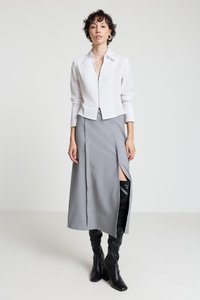 White cropped zip-up blouse with long sleeves, paired with a gray maxi skirt featuring a front slit. Black knee-high heeled boots.