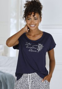 Námornícka košeľa s krátkym rukávom a bielym textom "Nech sa tvoje sny rozkvitnú" a kvetinovým vzorom; skombinovaná s bodkovanými pyžamovými dvojdielmi. Mäkká látka, voľný strih.