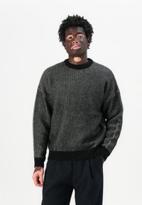 Maglione lavorato a maglia bianco e nero con un motivo testurizzato, vestibilità rilassata, polsini e scollatura a coste, abbinato a pantaloni scuri.