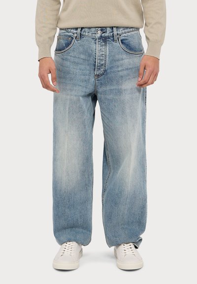 Ανοιχτό μπλε τζιν παντελόνι με άνετη εφαρμογή, που διαθέτει ψηλή μέση, μπροστινές τσέπες και ήπια φθορά. Συνδυάζεται με λευκά αθλητικά παπούτσια.