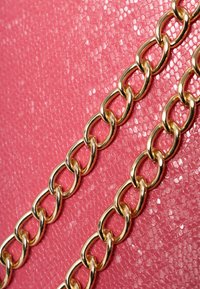 Eslabones de cadena de oro sobre un fondo texturizado rosa. La cadena presenta eslabones ovalados con un acabado brillante, en contraste con la superficie mate.