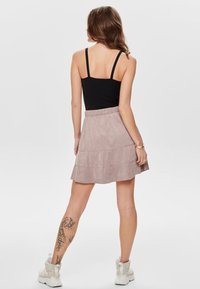 Světle růžová, vrstvená mini sukně s elastickým pasem, vyrobená z měkkého materiálu podobného suede. Nosit s černým tílkem a bílými kotníkovými botami.