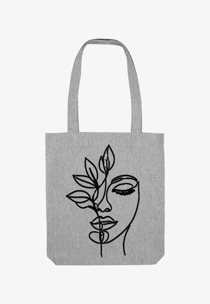 Grijze stoffen tas met een zwart geborduurd ontwerp van een gezicht dat verstrengeld is met bladeren, platte vorm en twee lange handvatten.