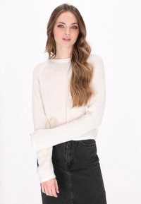Sweter dzianinowy w kolorze kremowym, z długimi rękawami i ściągaczami, zestawiony z czarną spódnicą dżinsową. Miękka tekstura i luźny krój.