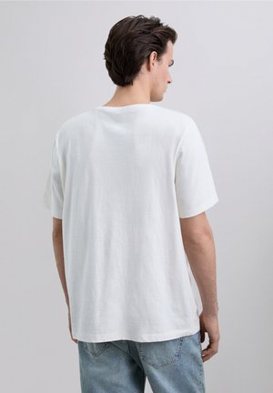 Camiseta blanca de manga corta hecha de una tela texturizada, con un corte relajado y escote redondo, combinada con jeans de mezclilla azul claro.