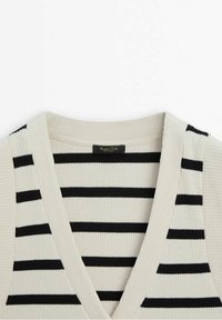 Sweter dzianinowy w kremowym kolorze z czarnymi poziomymi paskami. Posiada dekolt w kształcie litery V oraz prążkowaną fakturę. Metka marki widoczna na linii szyi.