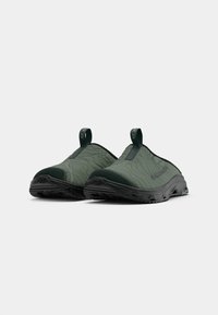 Grønne slip-on sko med quiltet tekstur, en robust gummisåle og en løfteløkke for enkel påkledning. Designet inkluderer subtil merking.