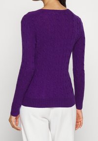 Pull en maille torsadée violet avec un ourlet et des poignets côtelés, présentant une coupe ajustée. Tissu texturé avec des manches longues et un col rond.