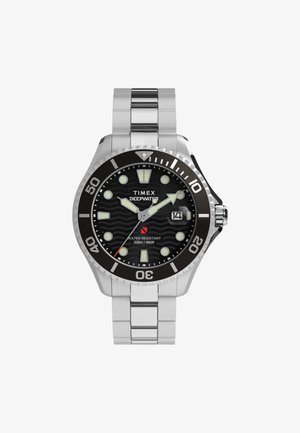 Timex Deepwater pulkstenis piedāvā nerūsējošā tērauda siksnu, melnu viļņu raksta ciparnīcu, gaismas indikators un rotējošu rāmīti ar dziļuma marķējumiem.