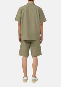 Olivenfarbene Kurzarmbluse und passende Shorts, beide aus einem strukturierten, leichten Stoff, kombiniert mit weißen und grauen Sneakern.