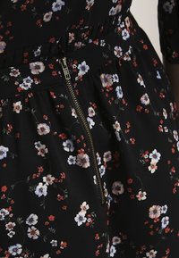Musta kukallinen mekko, jossa on hieno kukkakuosi punaisena, sinisenä ja valkoisena, vetoketjusuljenta ja poimutettu rakenne vyötäröllä.