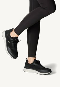 Schwarze Sportliche Schuhe mit einem atmungsaktiven Mesh-Obermaterial und gepolsteter Sohle, ausgestattet mit Schnürsenkeln und einer strukturierten Oberfläche. Kombiniert mit schwarzen Leggings.