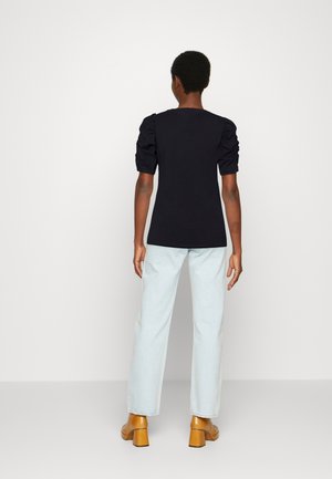 Sort tætsiddende t-shirt med puffede ærmer, kombineret med lyseblå jeans med lige ben og brune sko med blokhæl. Enkel og klassisk design.