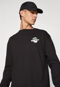 Black long-sleeve t-shirt with a round neck featuring a small, colorful graphic of a character wearing a straw hat on the left chest.