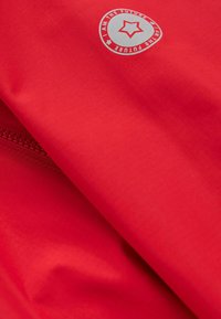 Tissu rouge avec une texture subtile en quadrillage et un logo circulaire comportant une étoile et le texte « I AM THE FUTURE » en blanc.