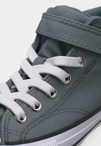 Γκρι αθλητικό παπούτσι με λευκά κορδόνια και μεταλλικά παπούτσια, με ραμμένο ύφασμα και ιμάντα βέλκρο πάνω από τα κορδόνια.