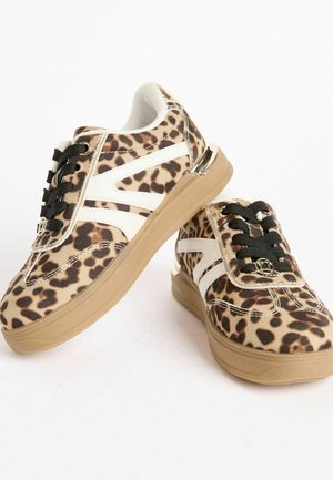 Tenisky s leopardím vzorem, béžovým textilním svrškem, bílými detaily, černými tkaničkami a strukturovanou béžovou podrážkou, s dekorativním kovovým prvkem.