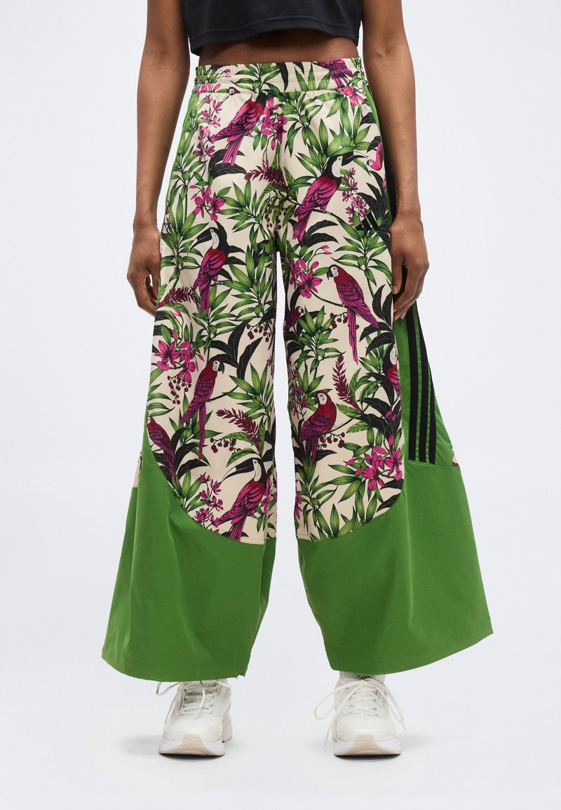 Pantalones de pierna ancha con estampado de pájaros tropicales y flores rosas, paneles inferiores verdes, combinados con zapatillas blancas y un top corto negro.