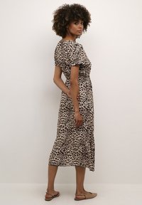 Leopardmönstrad klänning med korta ärmar och figurnära midja, med en utsvängd nederkant. Tillverkad av mjukt, lätt tyg. Bruna sandaler.