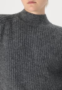 Gray ribbed knit sweater with a high neckline and textured finish, showcasing a soft, fuzzy material and structured shoulders.
