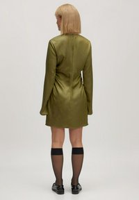 Groene satijnen mini-jurk met lange mouwen, gladde textuur en een getailleerde silhouet. Draag het met kniehoge zwarte sokken en zwarte schoenen.